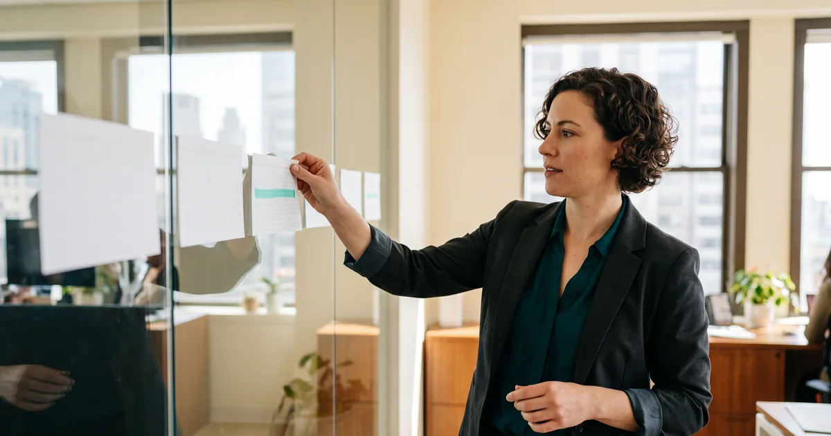 Healthcare operational leader arranging patient access workflow cards on a glass planning board