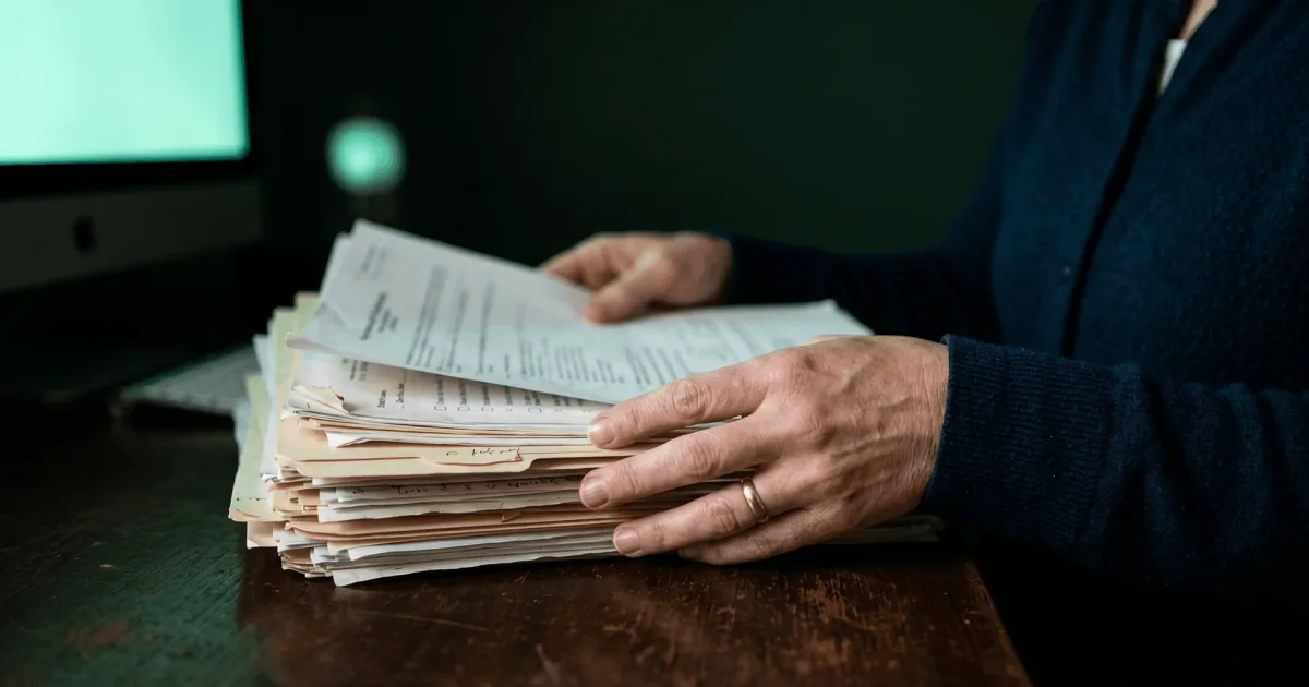 Coordinator sorting a stack of prior authorization paperwork at a desk